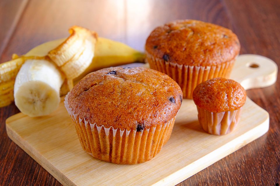 Banana muffin on a wooden board with a peeled banana in the background.
