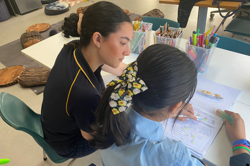 Head Start educator sitting with a young student, offering guidance and encouragement while helping with homework at school.